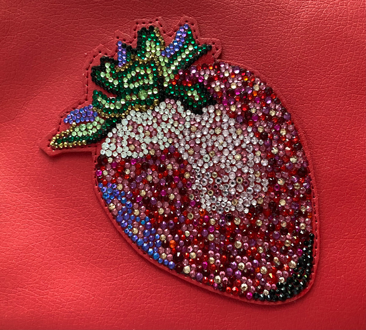 Detailaufnahme der handgesetzten Glas-Strasssteine der Strawberry Clutch in Pink, Rottönen, Grün und Gold
